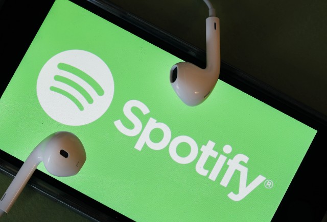 Un móvil con el logo de Spotify ocupando toda la pantalla y dos auriculares encima